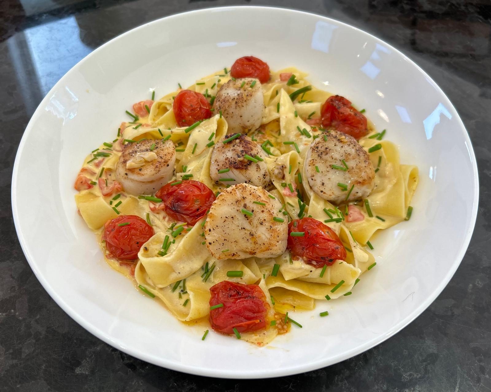 White plate with cooked pasta, tomato and scallop dish.